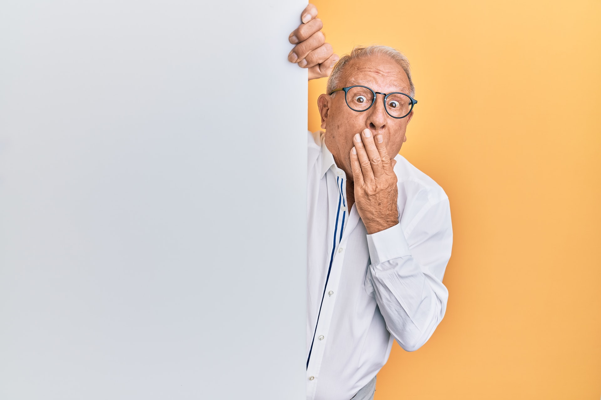 Surprised older man peeks out from behind a wall