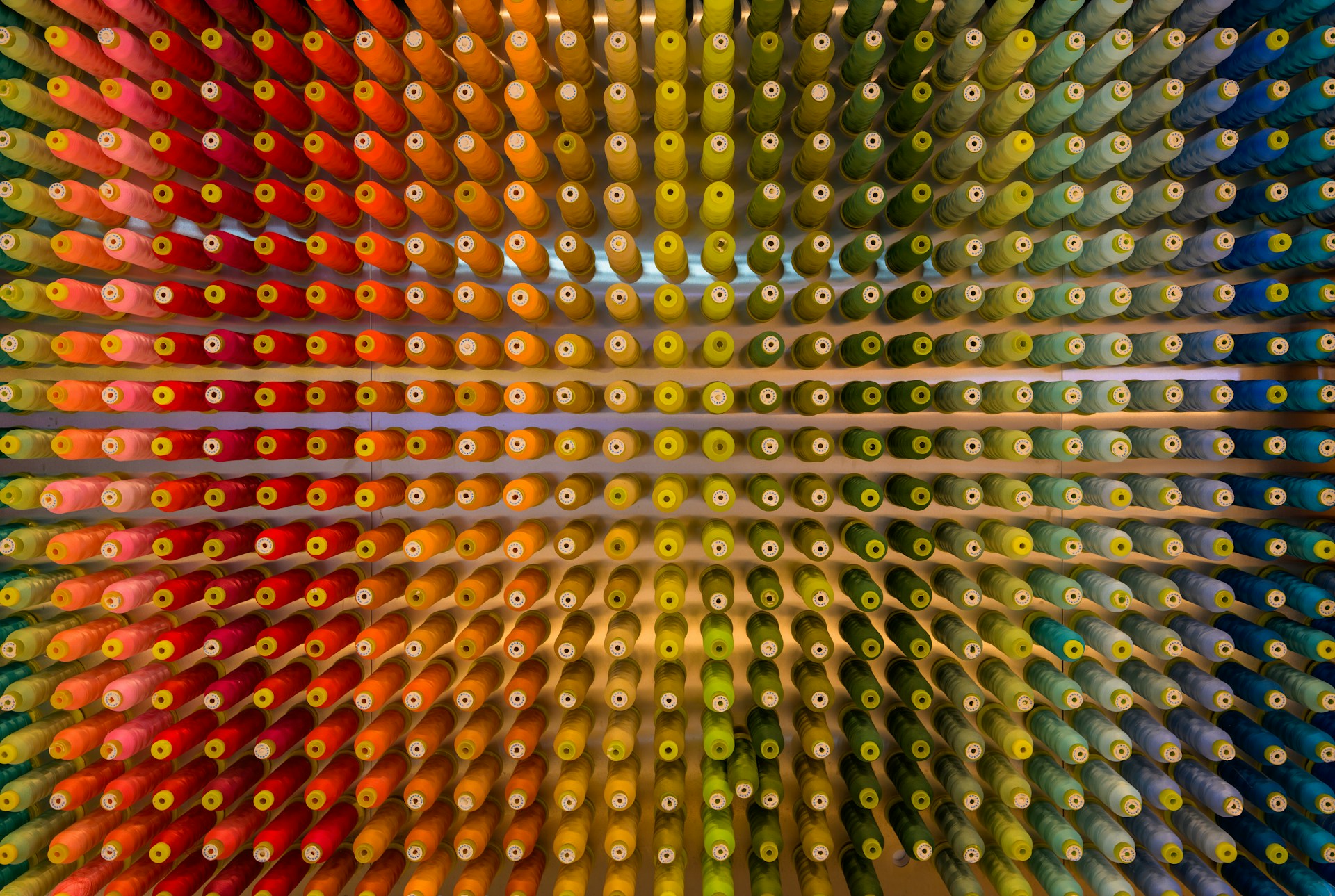 A rainbow of spools of thread organized on a wall